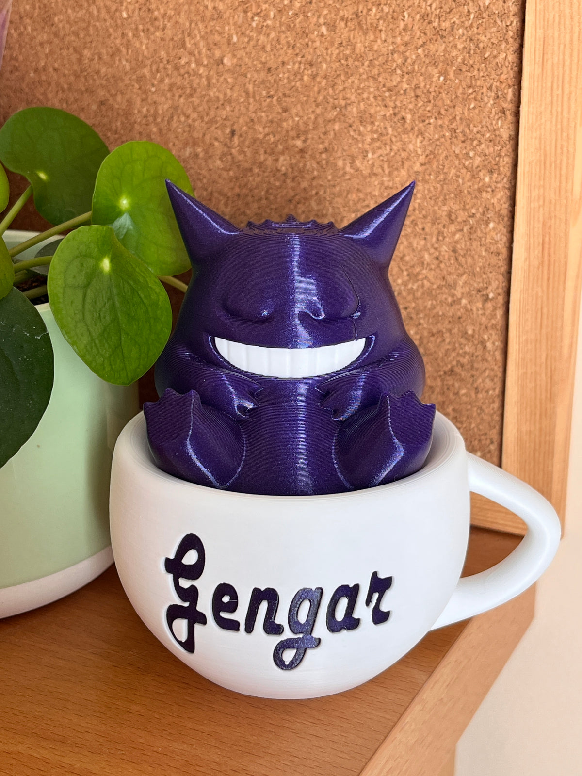 Figura decorativa de Gengar dormido dentro de una taza blanca con detalles morados
